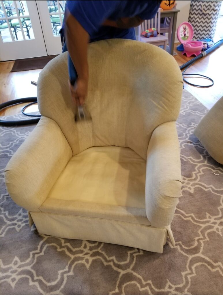 A man cleaning a chair in a living room.